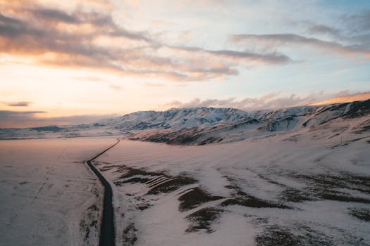 A serene winter landscape showing a snow-covered road through mountains at sunrise