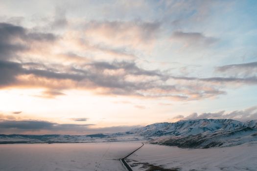 Aerial view of snow-covered mountains and road in Kosh-Agachsky, Altai, Russia at dawn.