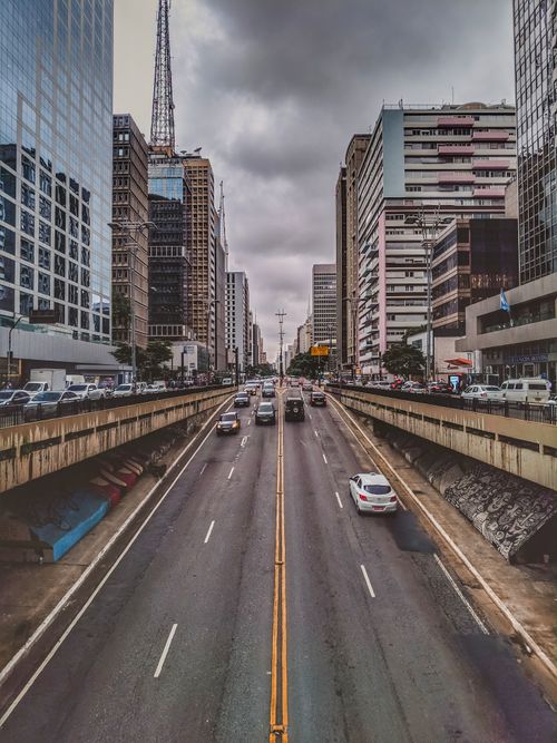 Free Perspective view of asphalt roadway with moving vehicles between modern multistory buildings of modern urban district under gray cloudy sky Stock Photo