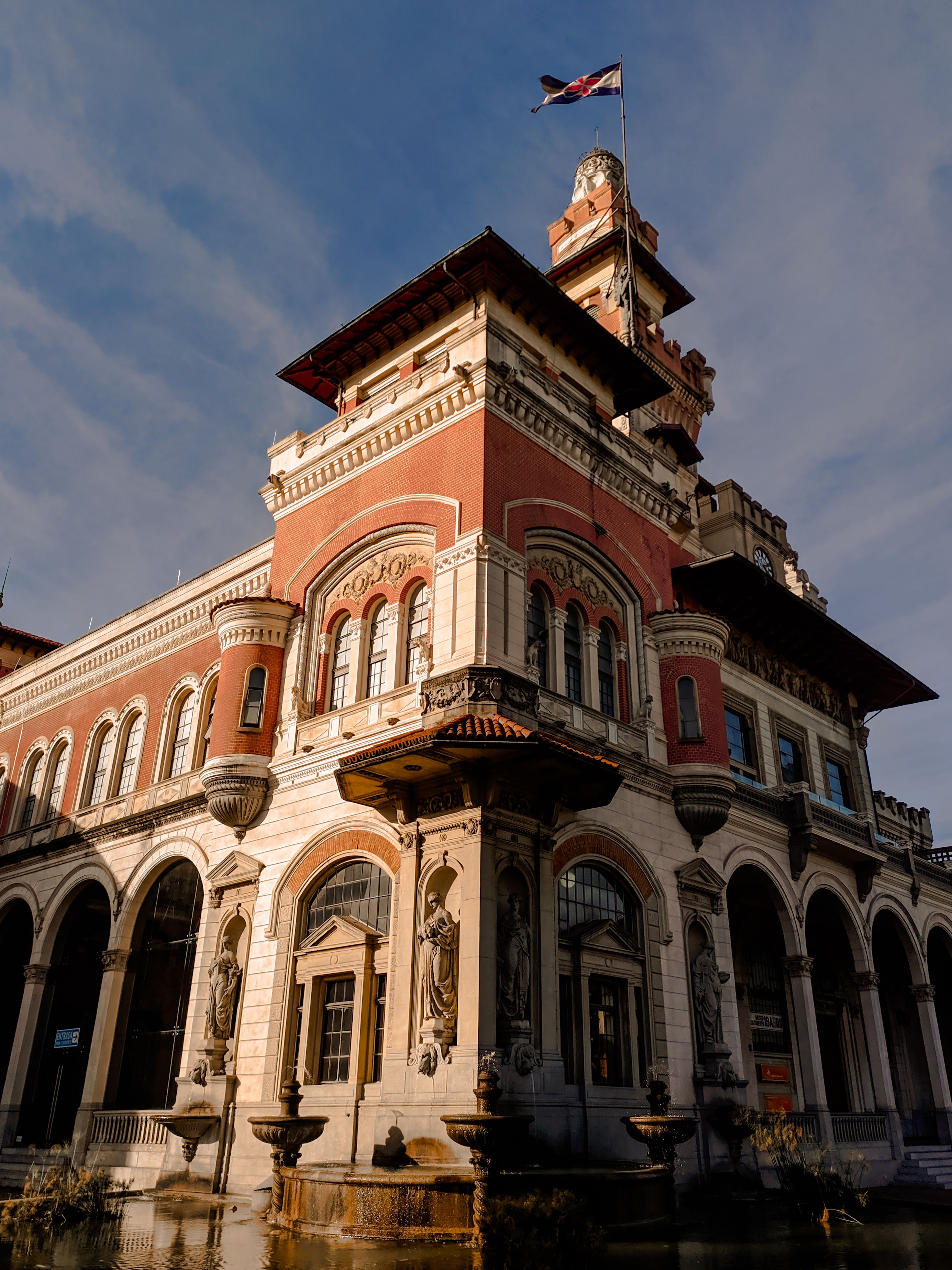 Low angle of old stone house exterior with ornamental elements and sculptures and with flag on roof against blue cloudy sky in city
