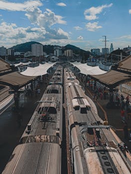 Aged trains on railway station against modern building facades and mountain under cloudy blue sky in town