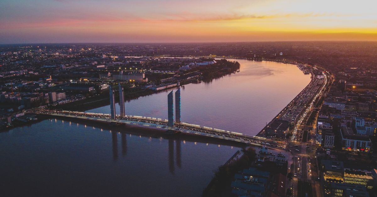 A stunning aerial view of Bordeaux's modern bridge and skyline at sunset over the Garonne River.
