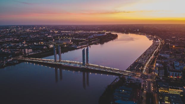 A stunning aerial view of Bordeaux's modern bridge and skyline at sunset over the Garonne River.
