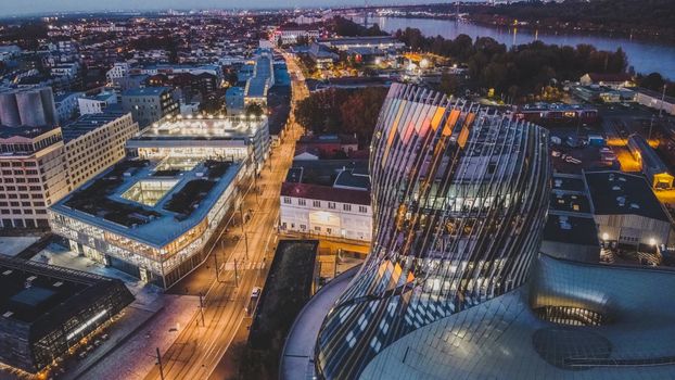 Dramatic nighttime aerial view of La Cité du Vin and surrounding urban landscape in Bordeaux, France.