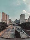 Vehicles driving on asphalt roadways between lush trees and high contemporary house facades under cloudy sky in city