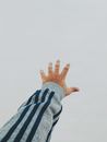 Crop unrecognizable lonely person in soft clothes with striped ornament reaching out arm on light background