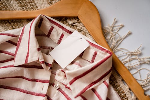 From above of casual shirt with red stripes and blank paper label placed on wooden hanger on rug