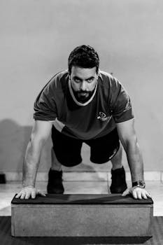 Grayscale image of a man doing a push-up exercise indoors using a block.