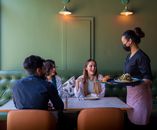 A diverse group of friends enjoy dining at a cozy restaurant in Bahrain, served by a waitress.