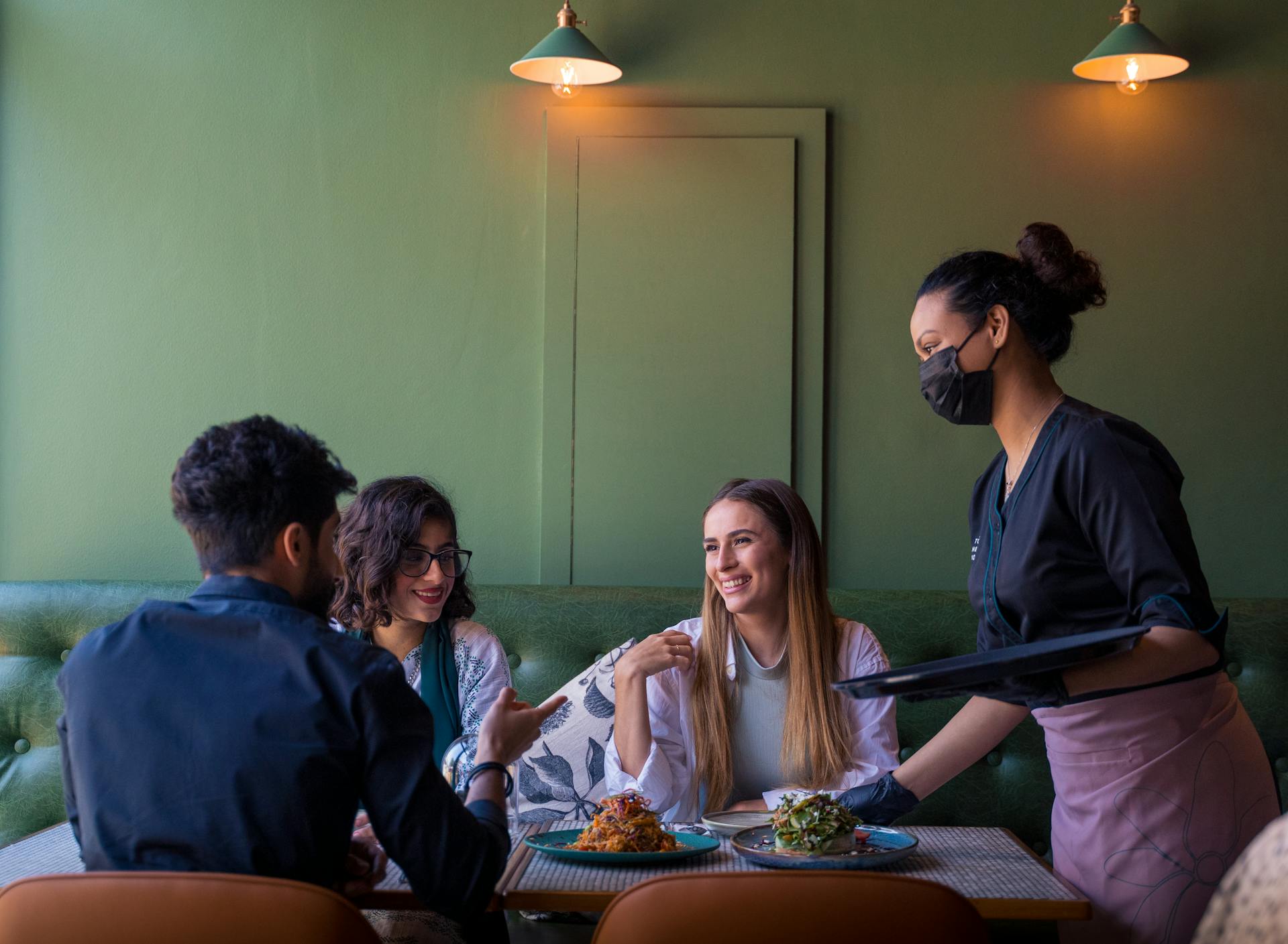 A lively group of friends enjoying a meal in a cozy Bahrain restaurant, served by a friendly waitress.