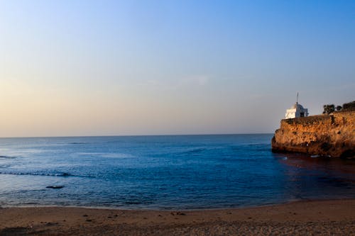 Белый маяк возле моря под голубым небом