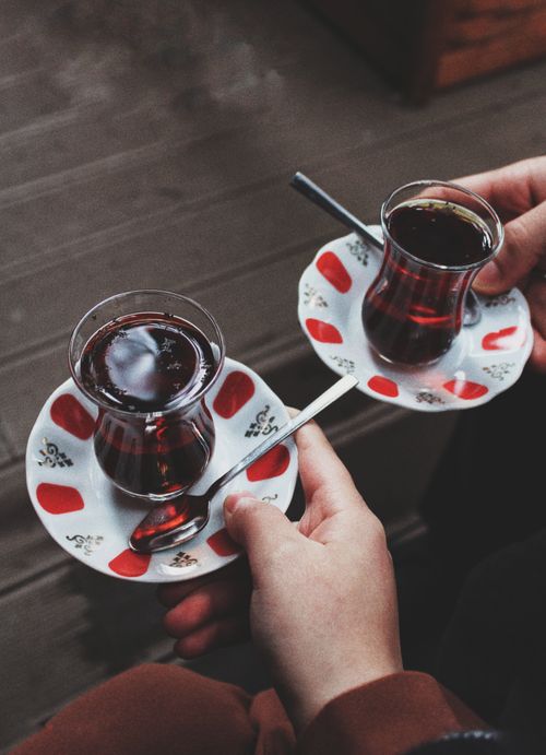 Free Close-up of hands holding traditional glass teacups served on decorative saucers for a warm tea experience. Stock Photo