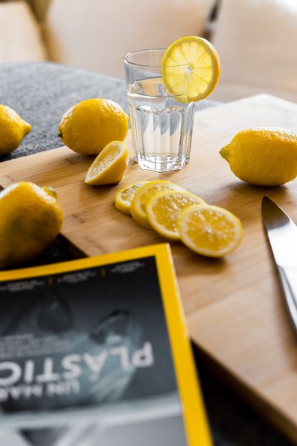 Glass of refreshing detox drink with lemon slice placed on wooden table with fresh fruit