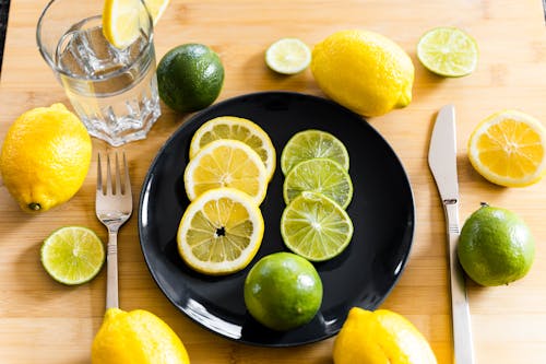 Fresh lemons and limes arranged on table with plate and water glass