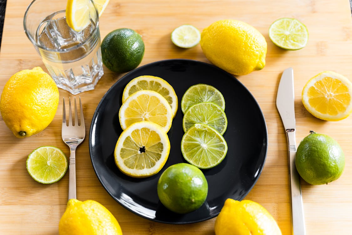 Free Fresh lemons and limes arranged on table with plate and water glass Stock Photo