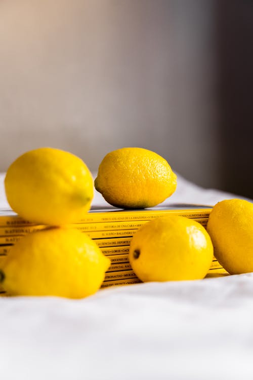 Free Fresh ripe whole lemons composed with stack of magazines on table covered with white tablecloth Stock Photo