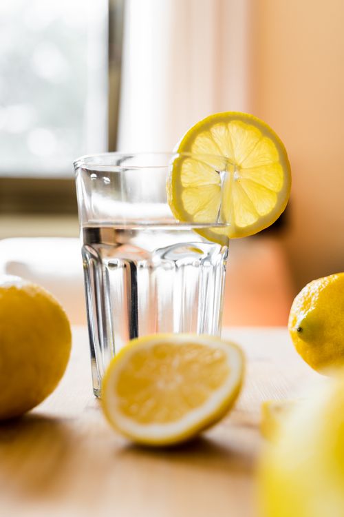 A glass of fresh water with lemon on a desk, part of learning how to drink more water every day