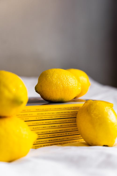 Fresh ripe whole yellow lemons placed on white cloth and stack of magazines on table in sunlight