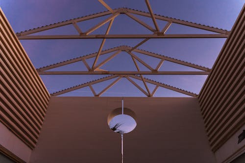 From below of contemporary building with ribbed walls and creative geometric construction on roof against purple sunset sky