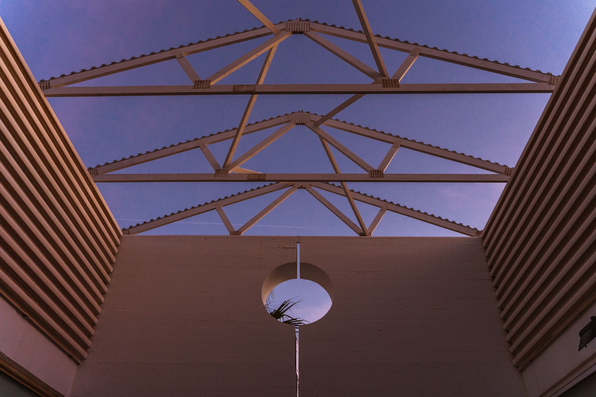 From below of contemporary building with ribbed walls and creative geometric construction on roof against purple sunset sky
