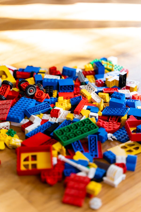 High angle heap of colorful plastic construction toys scattered on parquet floor in daylight at home