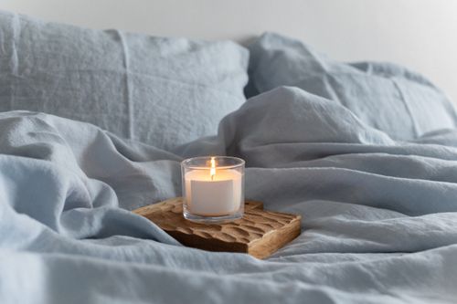 Free A soothing scene with a lighted candle on a wooden tray amidst soft blue linen bedding. Stock Photo