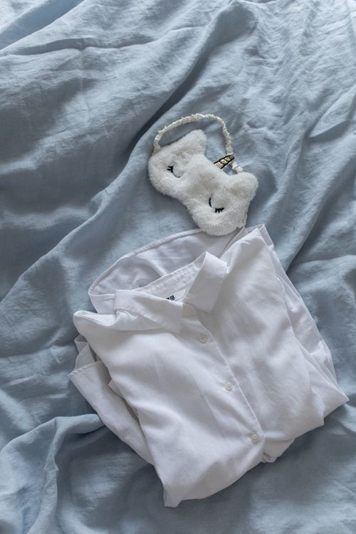 Free White linen shirt and sleep mask on soft blue bedding, creating a cozy and peaceful vibe. Stock Photo