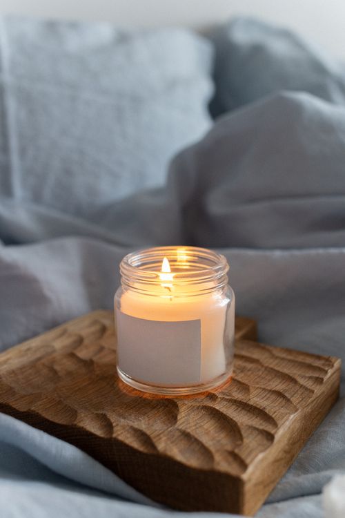 Free A warm scented candle on a textured wooden platform, creating a cozy ambiance indoors. Stock Photo