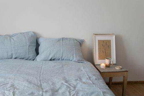 Free Tranquil bedroom scene featuring a cozy bed, soft linens, and a lighted candle on a wooden side table. Stock Photo