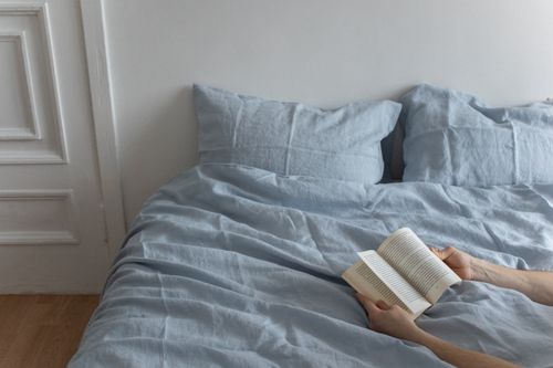 Free Cozy bedroom scene with linen bedding and a person reading a book. Stock Photo
