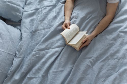 Free A person reading a book in a comfortable bed with light blue linens, creating a tranquil indoor setting. Stock Photo