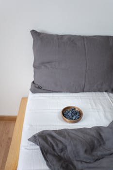 Minimalist bedroom setting with a bowl of blueberries on the bed, offering a touch of nature.