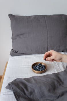 Hand reaching for fresh blueberries in a cozy bedroom setting. Perfect for healthy lifestyle themes.
