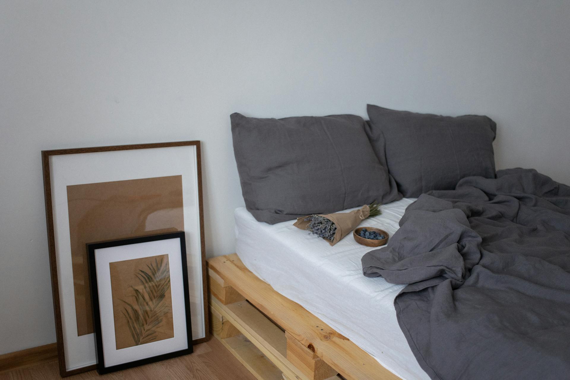 Stylish minimalist bedroom featuring grey bedding and framed art on wooden pallet bed.