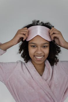 Cheerful woman wearing a pink bathrobe and sleep mask indoors.