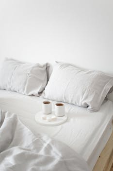 Cozy minimalist bedroom scene featuring coffee cups on a bed with white sheets, perfect for comfort themes.