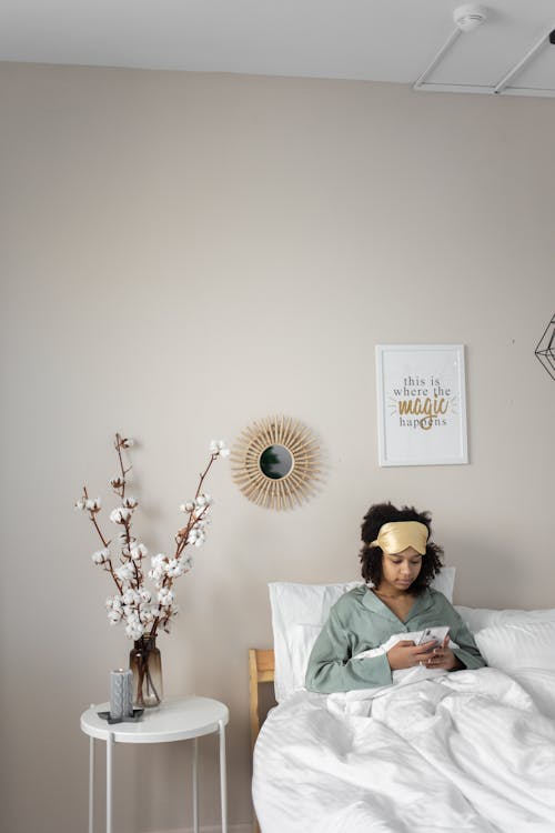 Free Woman in Pajamas Sitting on Bed while Using Cellphone Stock Photo