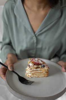 Close-up of a layered cake slice with fruits and nuts, held on a plate.