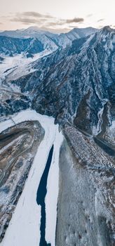 A breathtaking aerial view of a snow-covered mountain range and partially frozen river in Siberia's winter landscape.