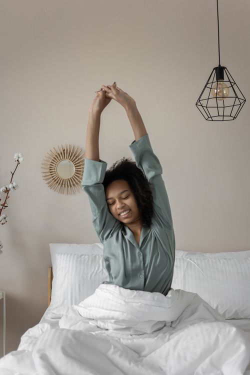 Free African American woman waking up, stretching arms in cozy bedroom setting. Stock Photo
