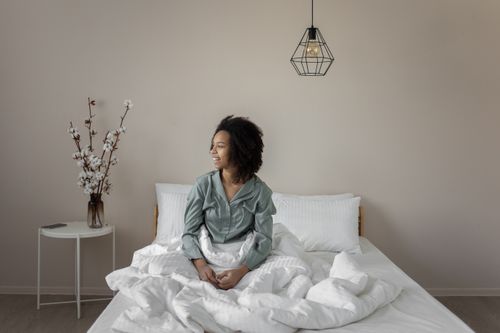 Free A young woman sits on a bed, exuding tranquility in a minimalist bedroom. Stock Photo