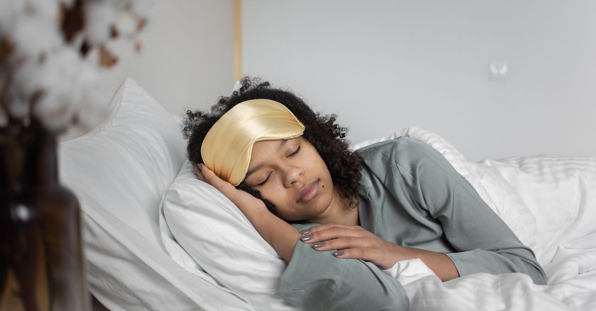 A young woman peacefully sleeps with a sleep mask, nestled in cozy white bedding. - Evidence evidence guide for golden kiwi sleep randomized trial