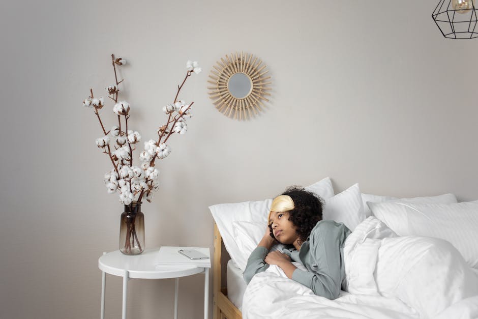 5 Hidden White Noise Machine Features for Better Sleep A woman relaxing in bed with a sleep mask, surrounded by white bedding and decor.