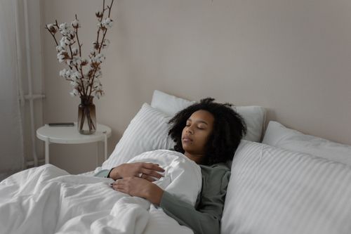 Free A woman resting peacefully in bed with a cozy blanket and soft pillows. Stock Photo