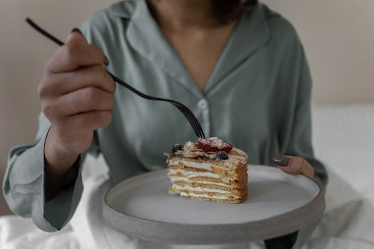 A person holding a plate with a slice of layered cake topped with berries, ready to eat.