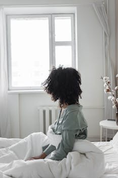 Woman with afro hair sitting in a bright bedroom, enjoying a morning view.