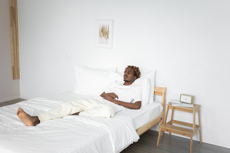 Saatva vs DreamCloud: Hybrid Support Showdown A man resting peacefully on a bed in a minimalist white bedroom interior setting.