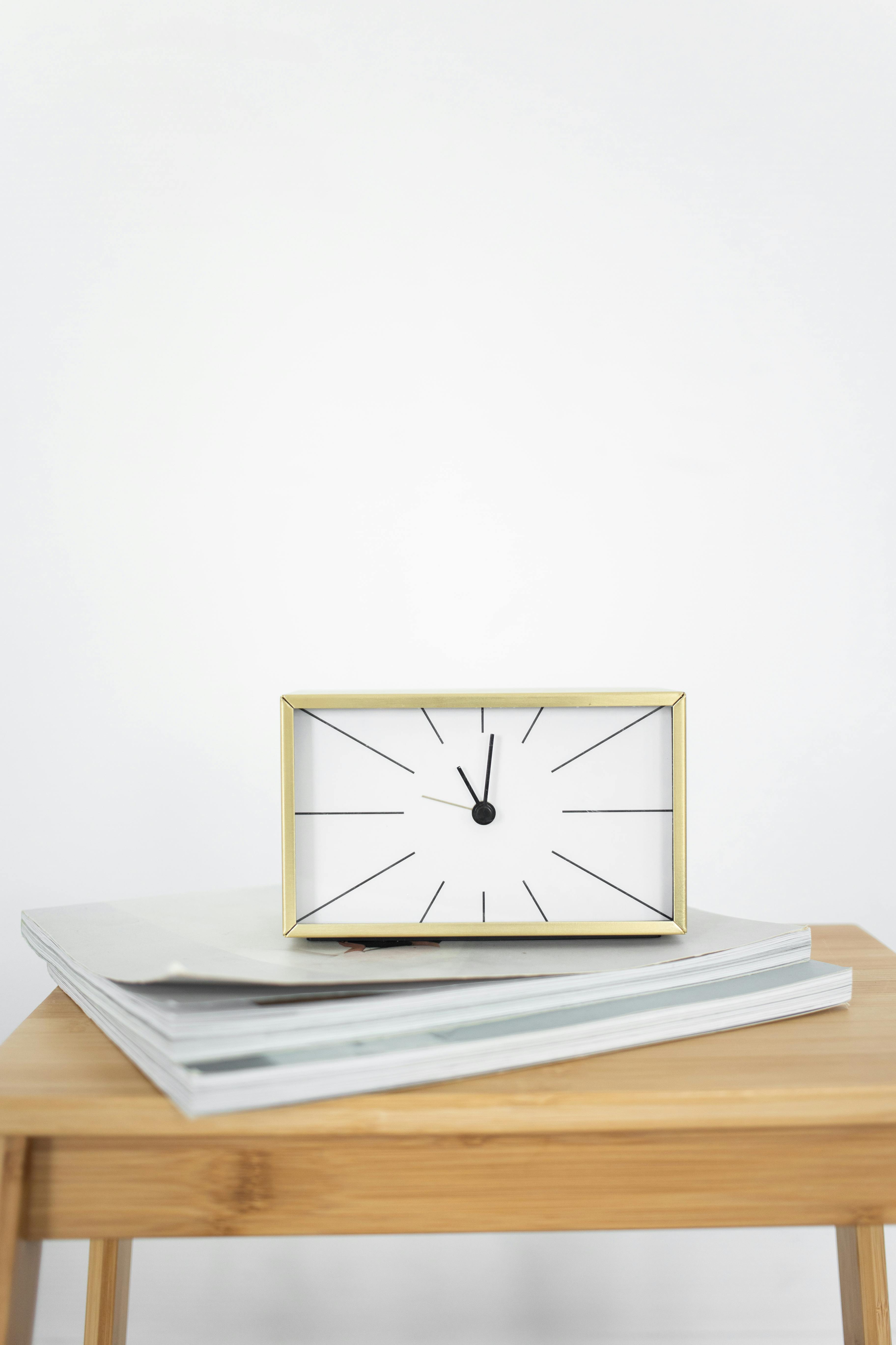 A minimalist rectangular clock placed on a stack of books on a wooden table.