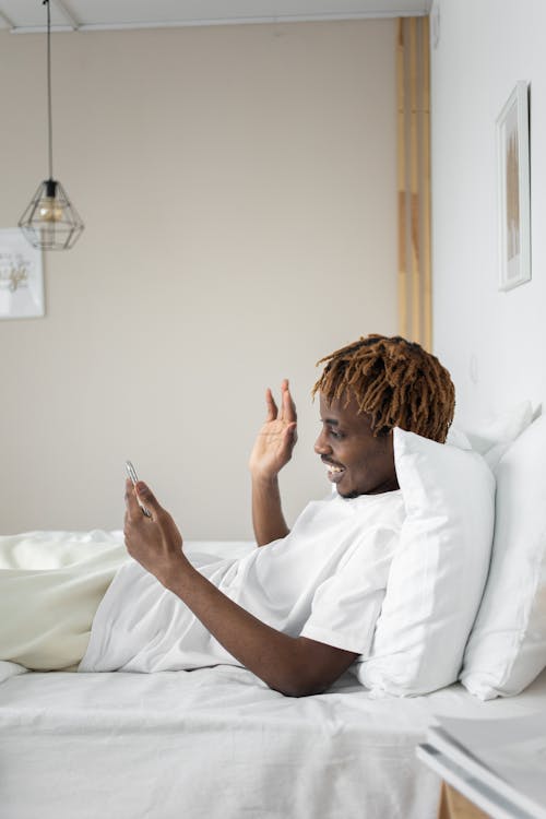 Free Man Waving Hand While Lying on Bed Stock Photo