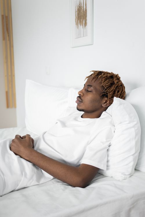Free African American man sleeping peacefully on a white bed indoors. Stock Photo
